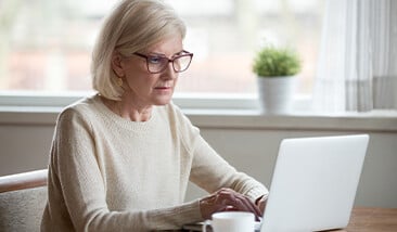 Older women in a tan sweater looking at her laptop contemplating a cremation decision