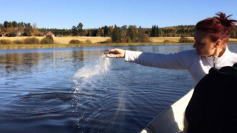 woman scattering cremains over water from a boat