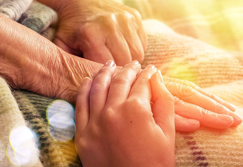 healthcare worker hands holding elderly person hands on top of blanket