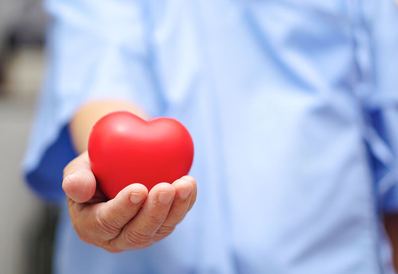 hospice care worker in blue scrubs holding red heart object in hand
