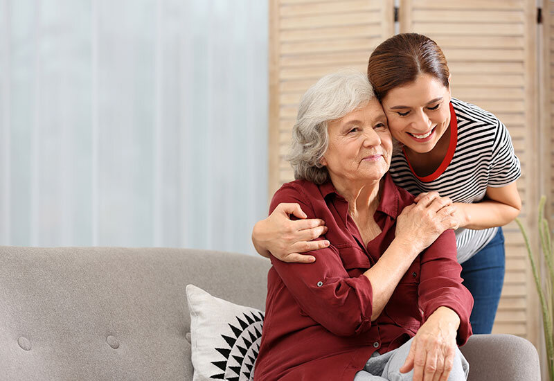 elderly mother and younger daughter embracing on couch at home