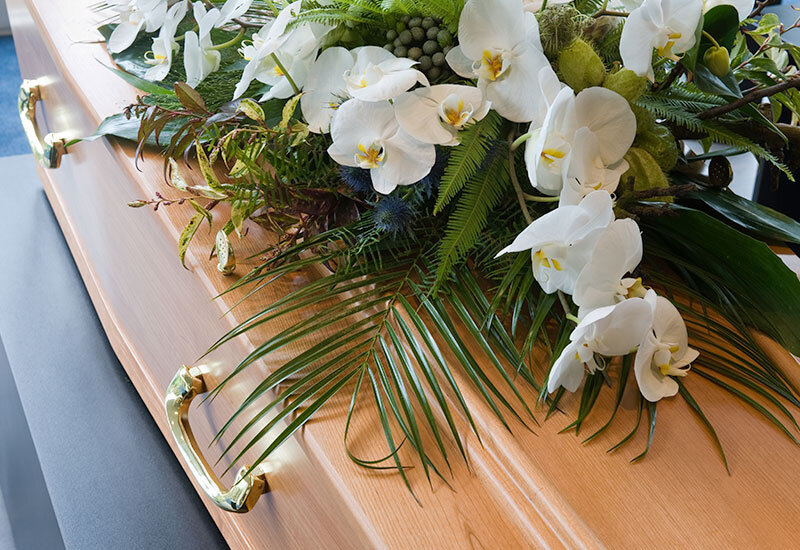 wooden coffin with brass handles and flower arrangement, sitting at crematorium
