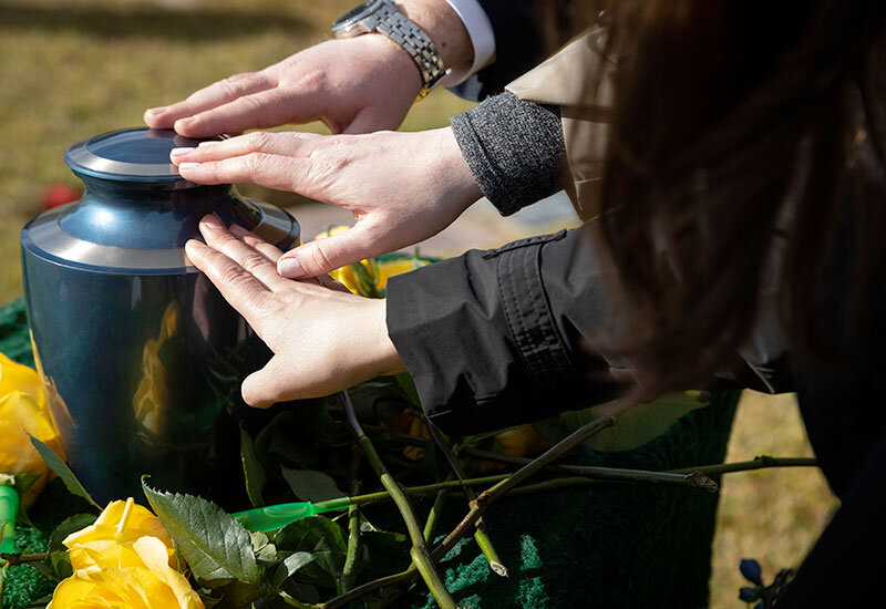 3 people's hands touching cremains urn at celebration of life service in San Diego