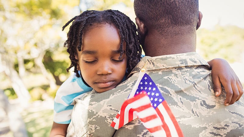 Army veteran holding young child who is holding a US flag at a memorial service