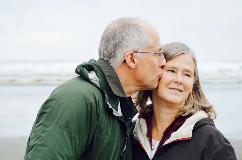 elderly man kissing his wife on southern california beach