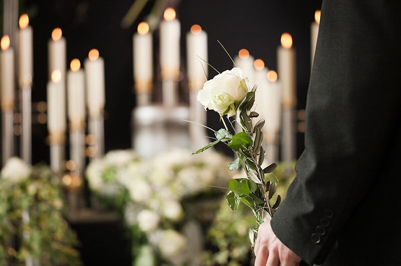 funeral service with candles, man holding flowers, during covid Jan 2022