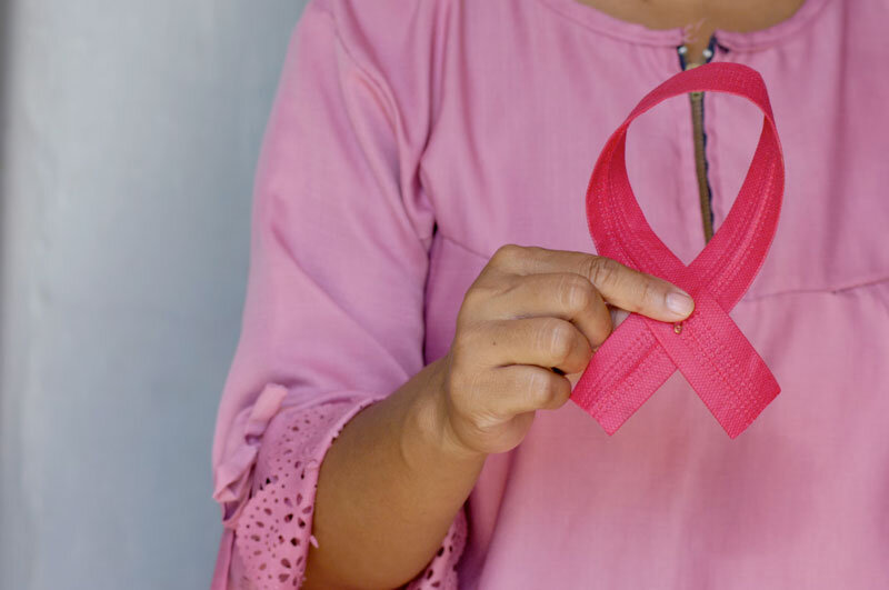 woman in hospice care wearing a pink gown holding a pink breast cancer awareness ribbon