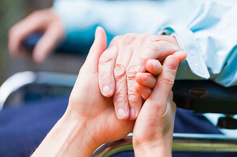 death doula holding hand of elderly person in wheelchair, close up view of hands