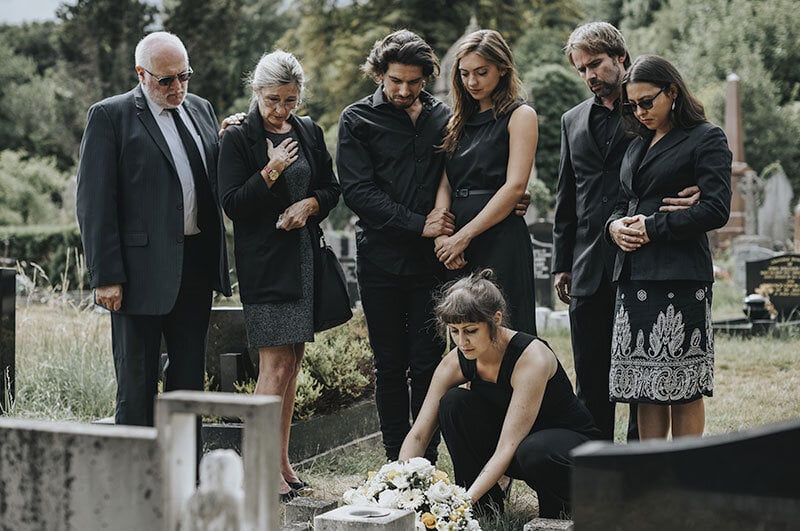 family at funeral placing flowers on grave of loved one