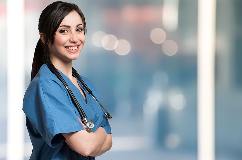 young woman nurse smiling and standing against wall in hospice care facility