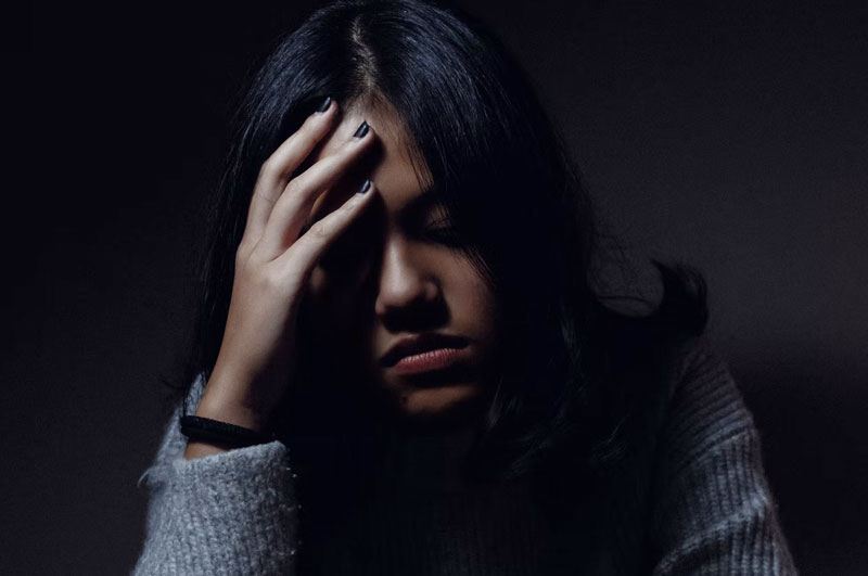 young woman in dark room holding head in hand while grieving a loss