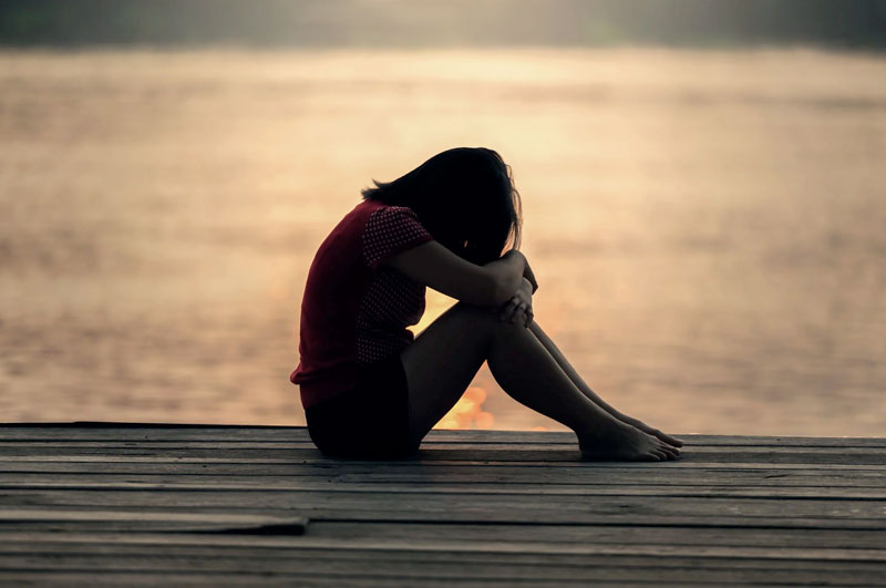young woman sitting on lake dock feeling grief or depression