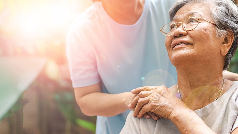 woman with hand on shoulder of elderly parent in hospice care, outdoors in California