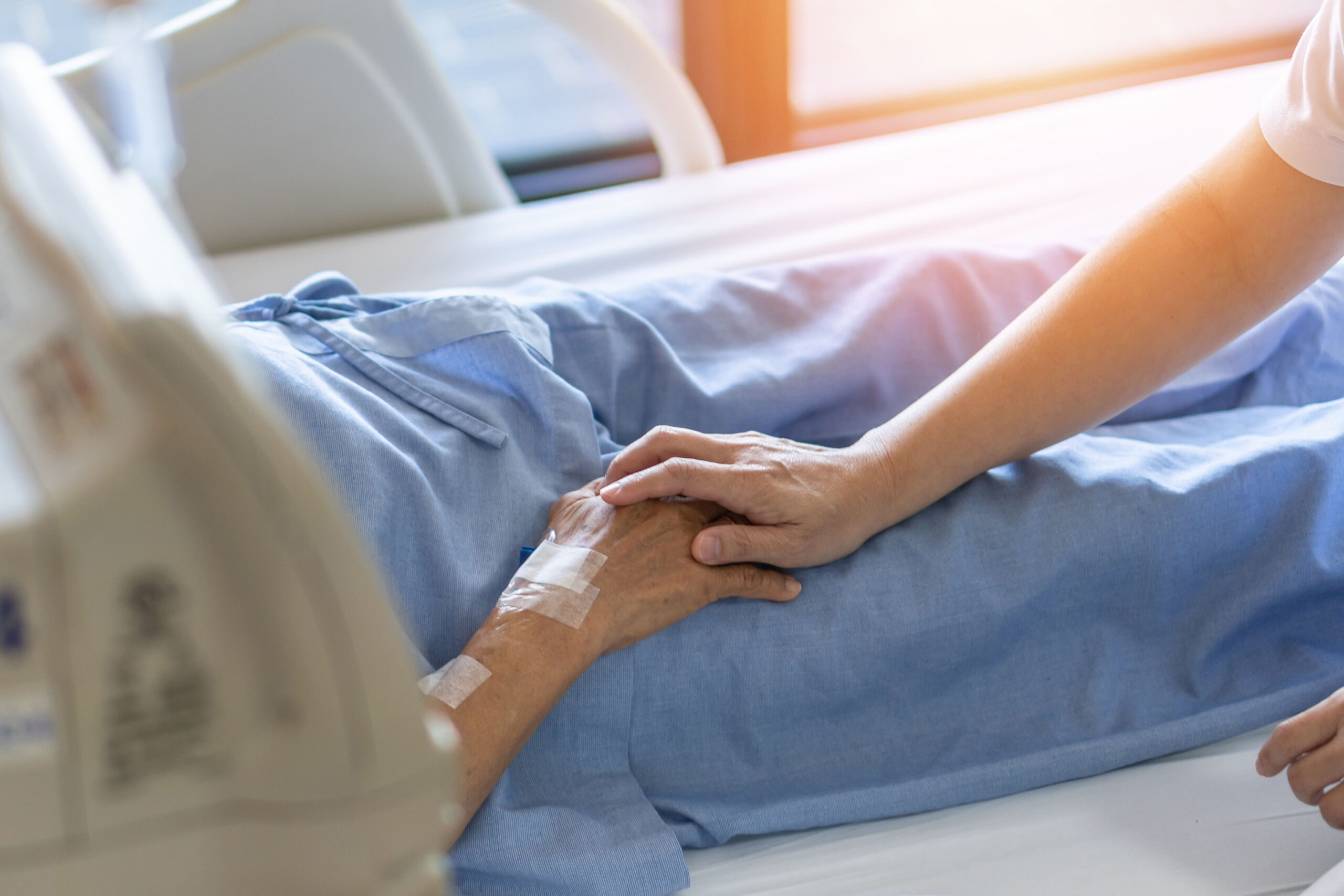A relative holds a loved one's hand as they say goodbye to someone in hospice care