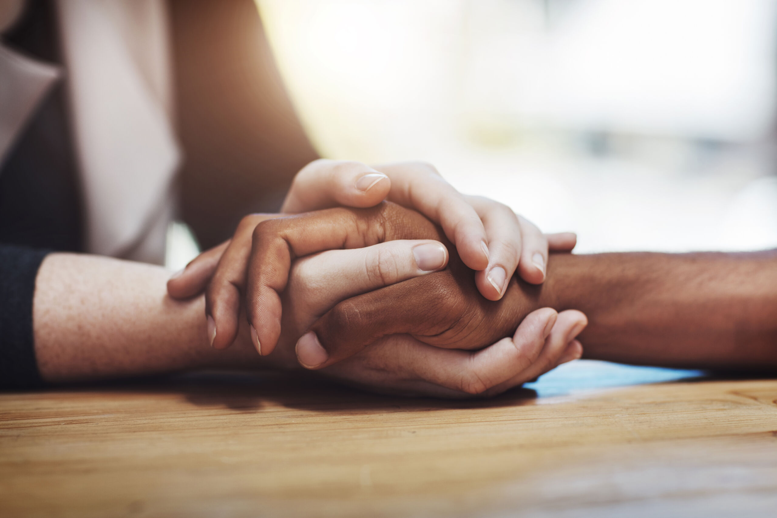 Support, compassion and trust while holding hands and sitting together at a table. Closeup of a loving, caring and interracial couple or friends comforting each other after a loss or cancer news.