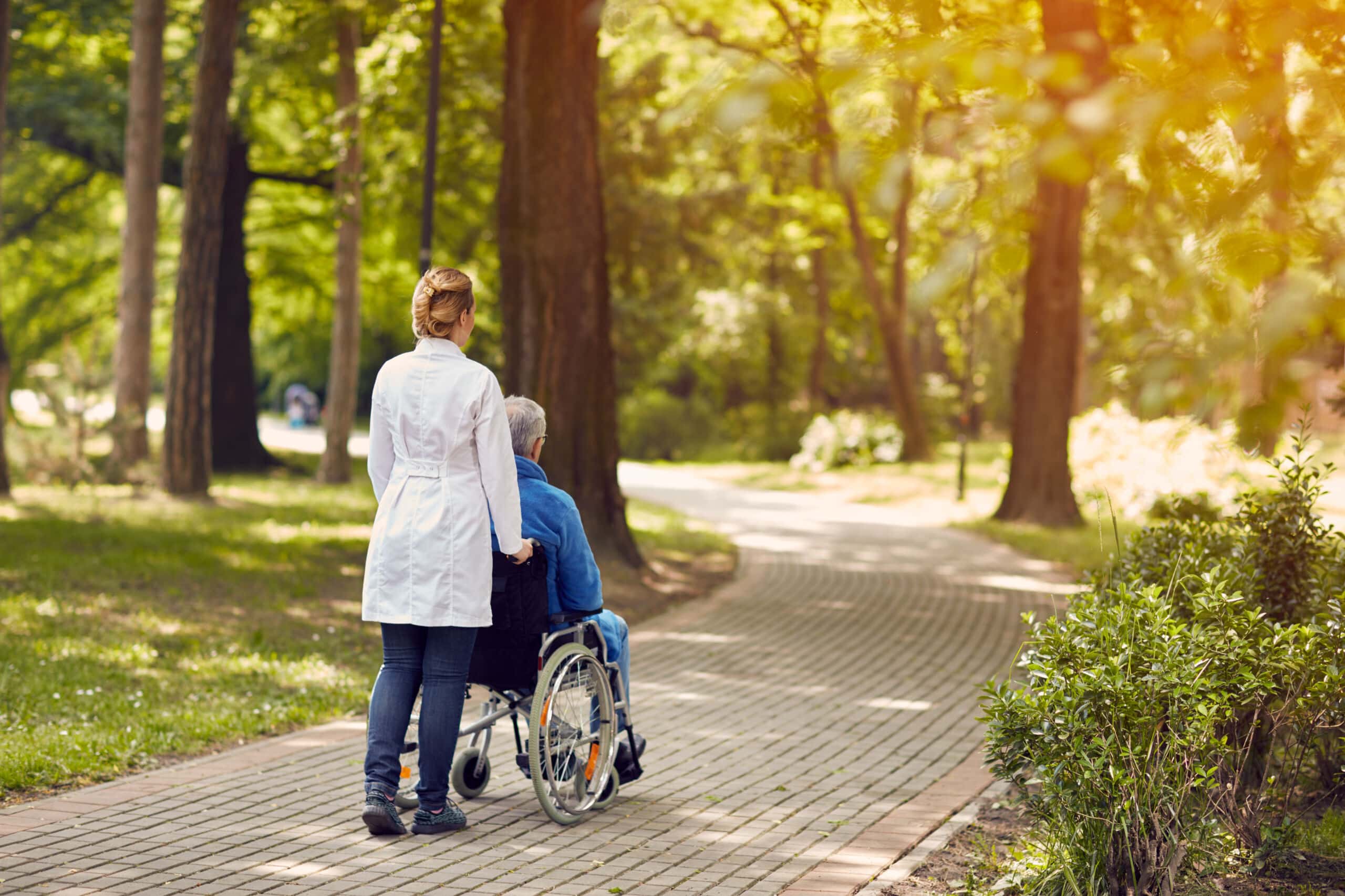 Hospice nurse helping elderly man on wheelchair outdoor