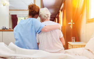 Nurse in hospice hugs elderly woman on bed for comfort while grieving